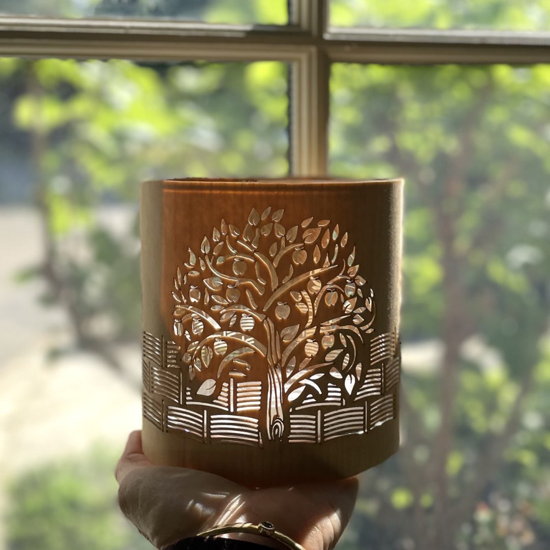 A candle holder or lantern with an apple orchard design held in front of a sunny window