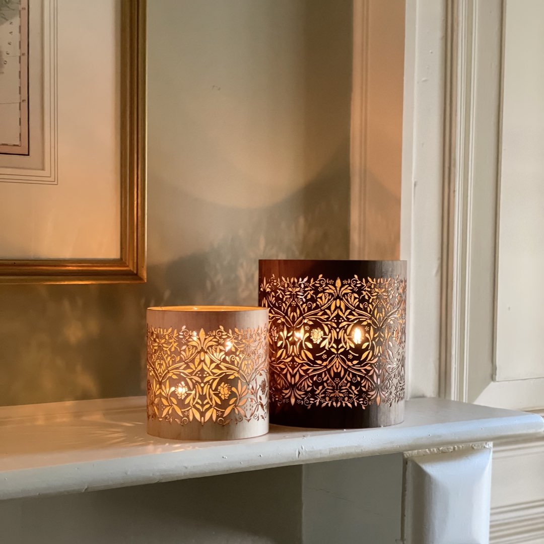 two candle holders inspired by william morris and his summer residence, Kelmscott. They are lit and sitting on a traditional mantle