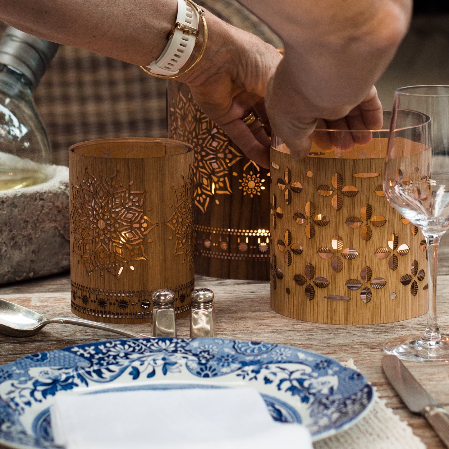 small oak mandala lantern with a large walnut mandala lantern on a wood table outside on the patio - blue Italian dishes putting the jojo cozy on to glass