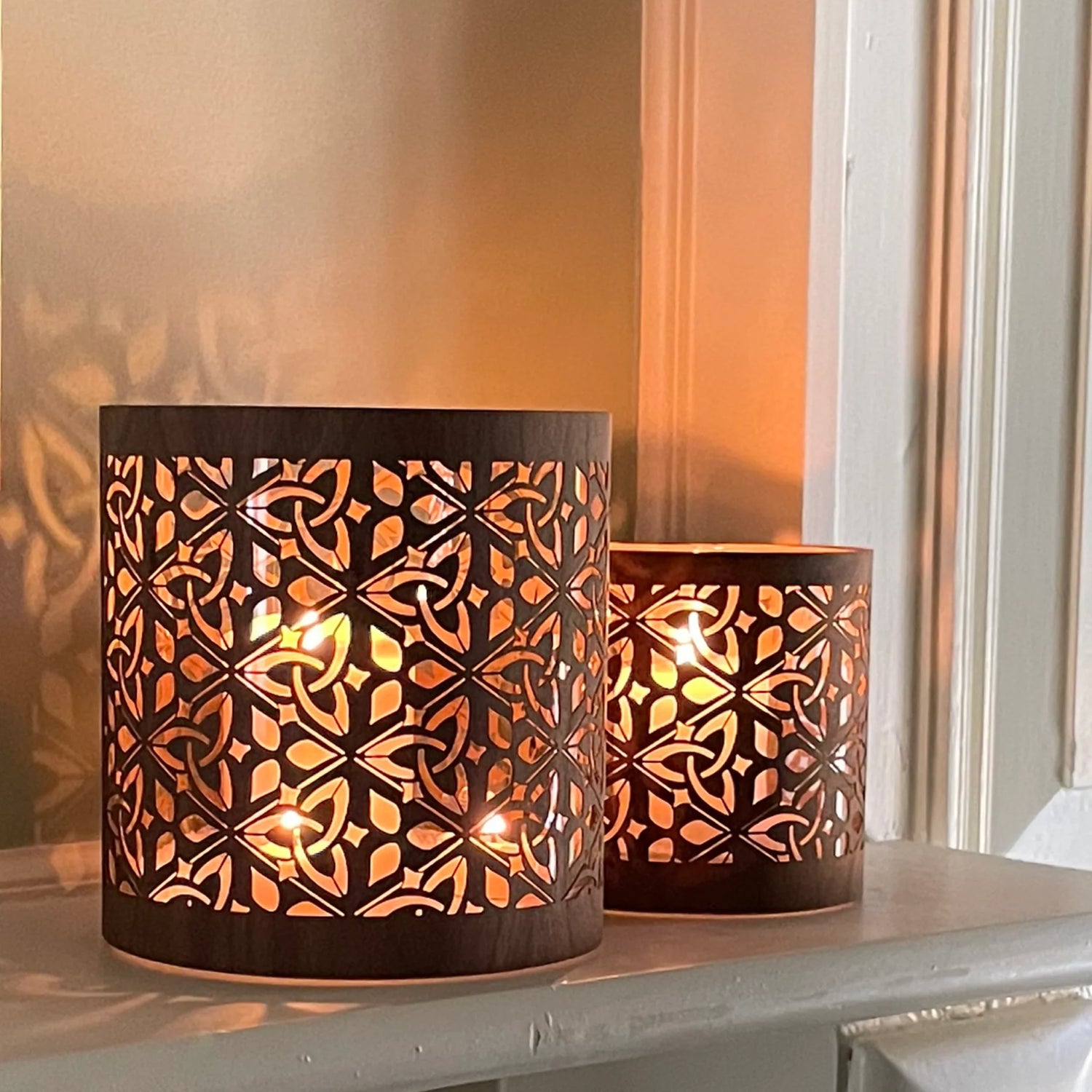 two cletric triquetra lanterns in black walnut sitting on a mantlepiecein 