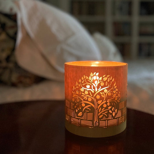 A candle holder or lantern with an apple  orchard design glowing softly besdie a bedside table
