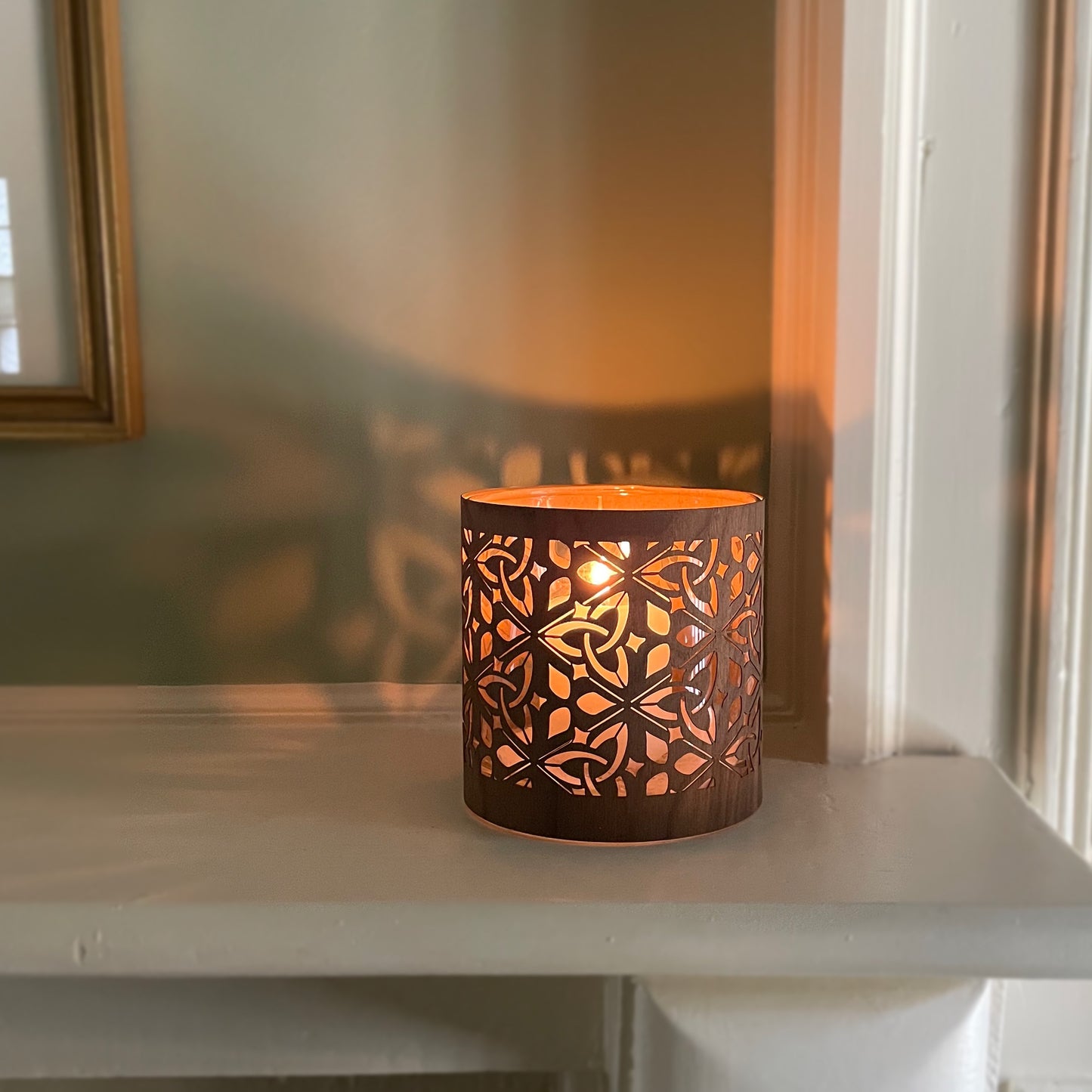 Decorative candle holder with intricate cut-out patterns - the deisgn is the celtic triquetra and the wood is black walnut veneer. The laantern is lit and the deisgn is reflecting on the wall behind