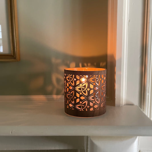 Decorative candle holder with intricate cut-out patterns - the deisgn is the celtic triquetra and the wood is black walnut veneer. The laantern is lit and the deisgn is reflecting on the wall behind