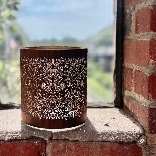 a william morris candle sitting on a brick window sill back lit by the sun