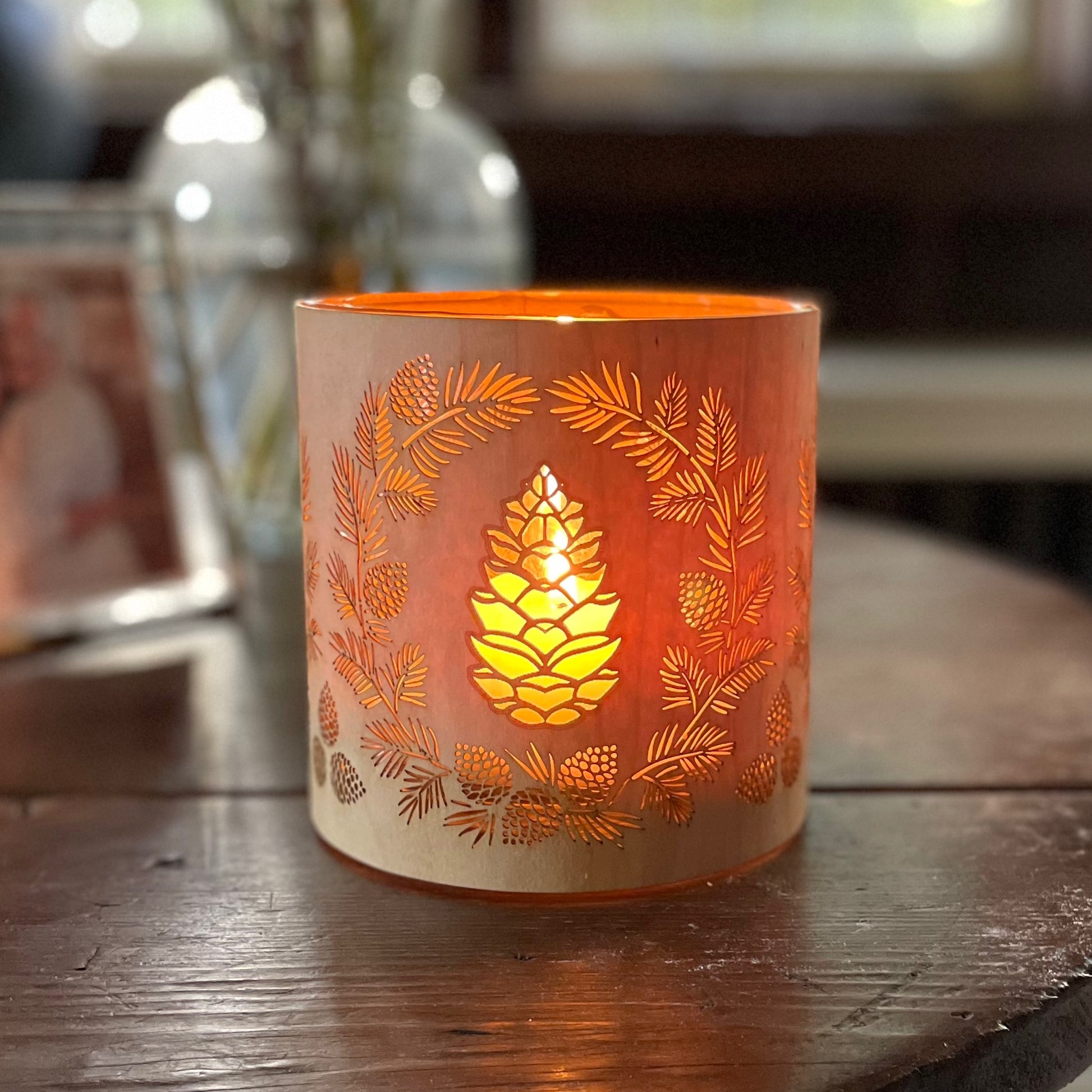 a glass lantern candle holder wrapped in maple veneer with laser cut pinecone design