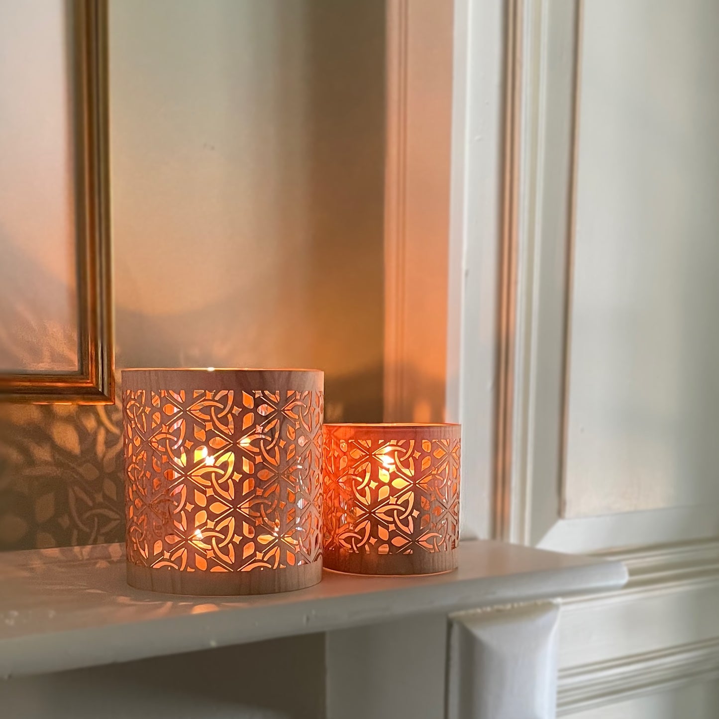 The large and medium size triquetra lantern in maple wood and heavy glass. Resting on a mantle with the design relecting on the wall behind