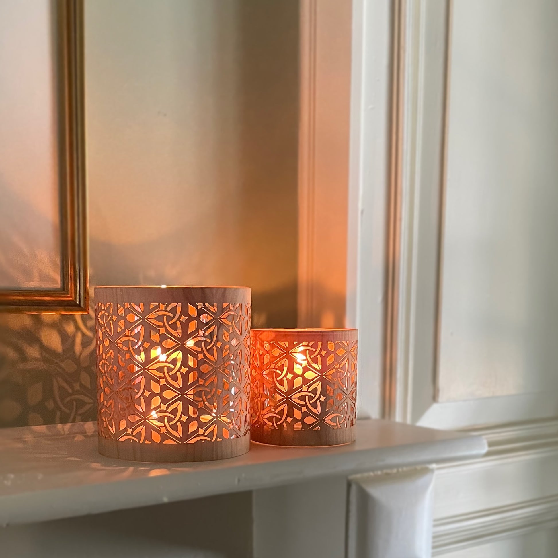 The large and medium size triquetra lantern in maple wood and heavy glass. Resting on a mantle with the design relecting on the wall behind