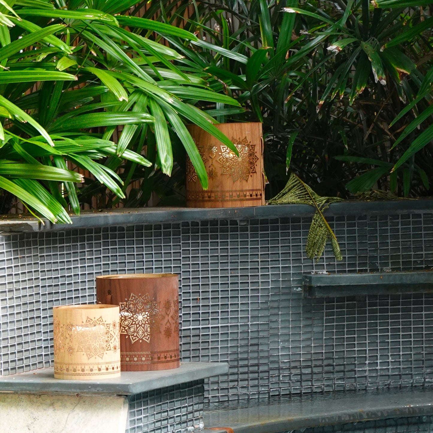 medium maple mandala lantern with a large walnut mandala lantern and a large maple mandala lantern on the ledge of a pool in the garden of a home in Key West Florida