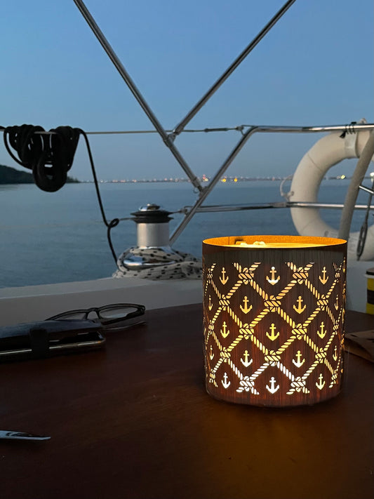 this is a luci light srrounded by a cozie kit with the nautical design sitting on the deck of a sailboat with the harbour in the background at dusk