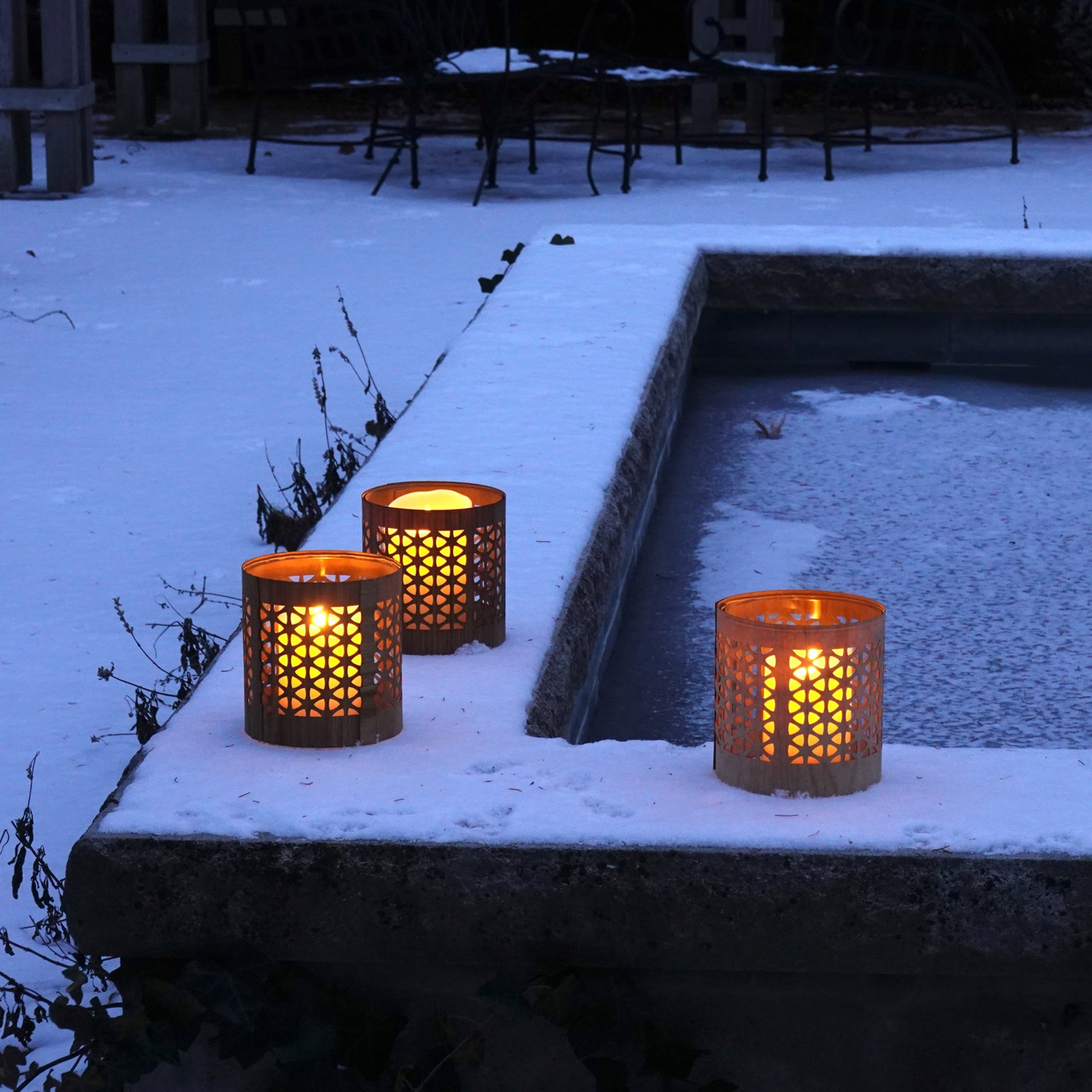three mid-century modern lanterns in the snow by a frozen hot tub